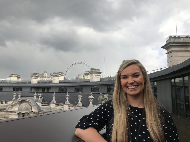 image of Faye standing on the balcony of the DCMS building with the London Eye in the background
